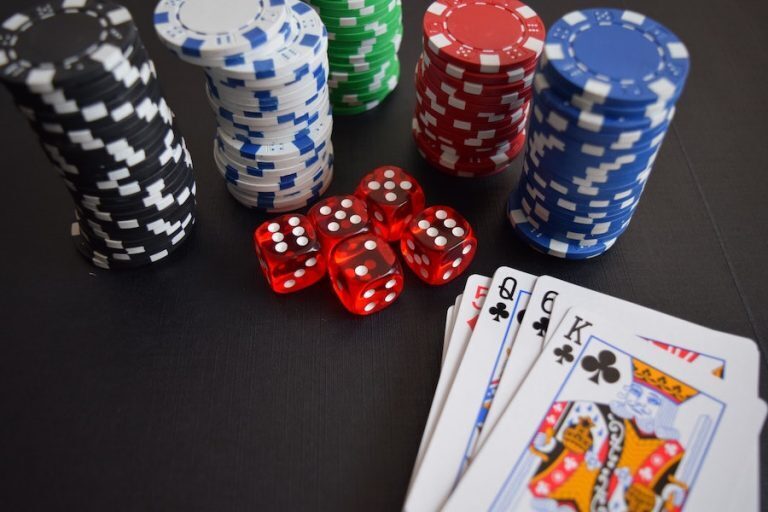 Poker chips, dice, and playing cards lie scattered on a sleek black surface